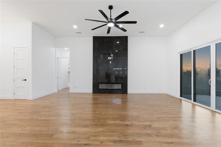 Unfurnished living room featuring a large fireplace, ceiling fan, light wood-style floors, and recessed lighting