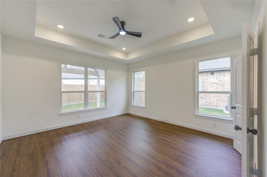 This bedroom is bright, spacious room with large windows, wood flooring,  and a ceiling fan.