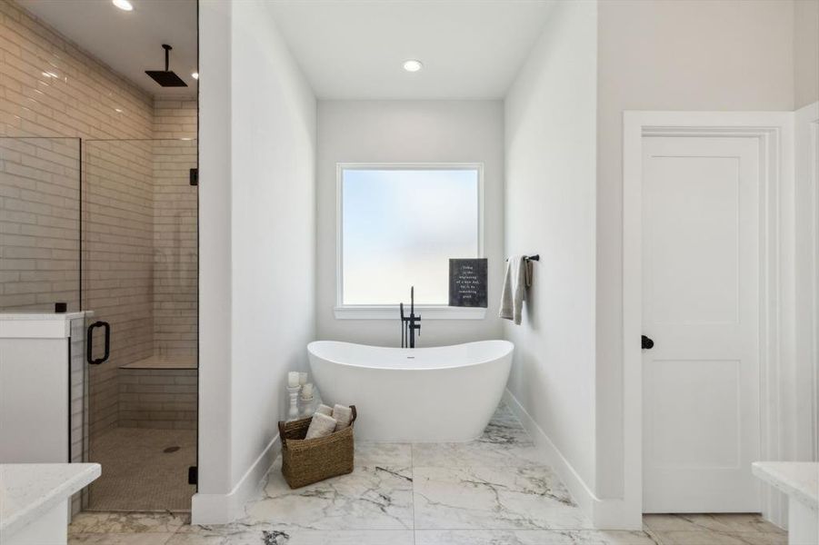 Freestanding soaking tub with a matte black floor-mounted faucet, complemented by large format marble-finish floor tiling