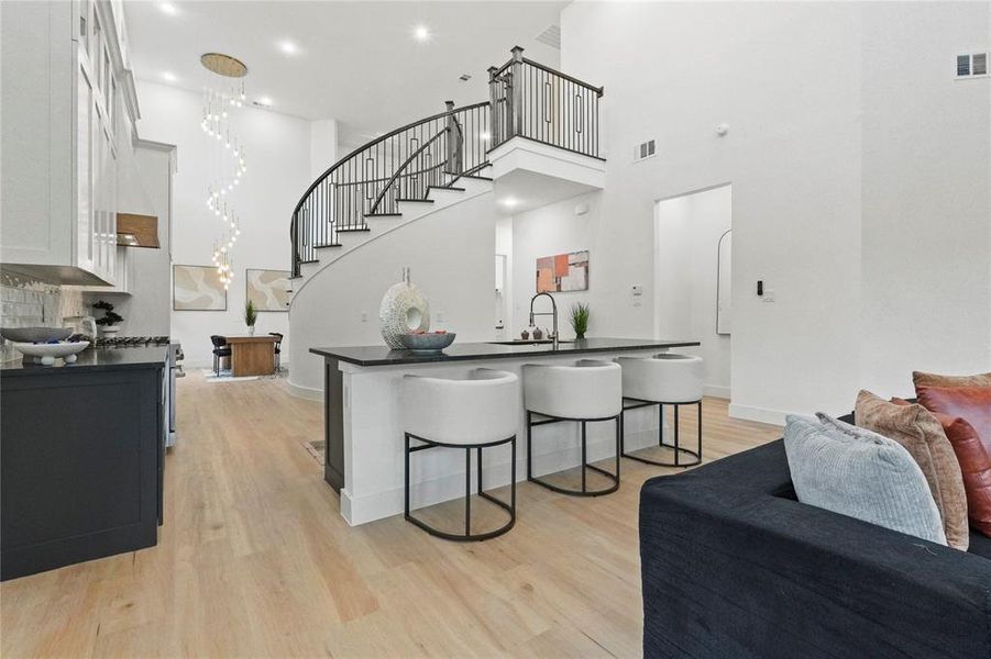 Kitchen featuring a kitchen bar, light wood finished floors, an island with sink, white cabinetry, and stainless steel range with gas cooktop Kitchen featuring a kitchen bar, light wood finished floors, an island with sink, white cabinetry, and stainless steel range with gas cooktop