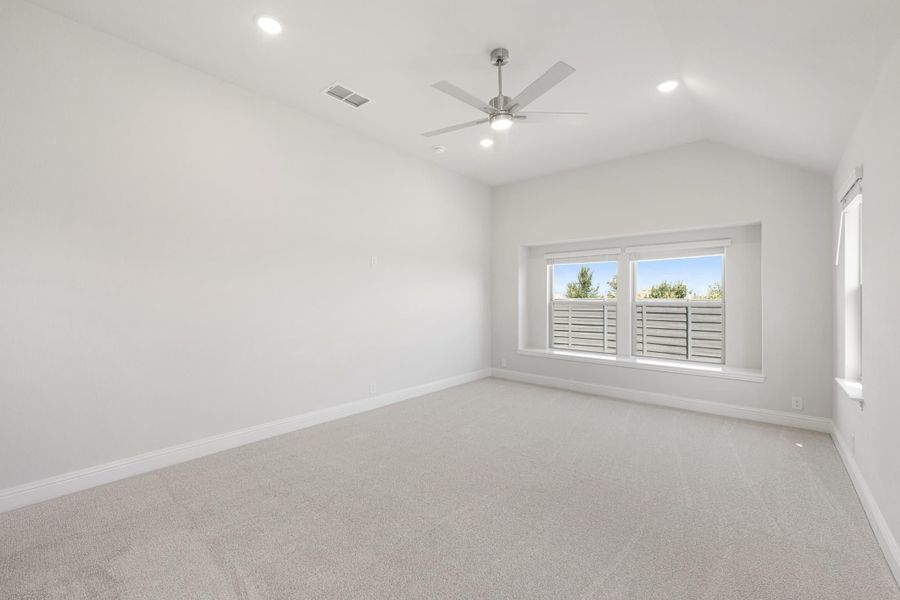 Empty bedroom with vaulted ceiling, ceiling fan, carpet flooring, and large window with outdoor view