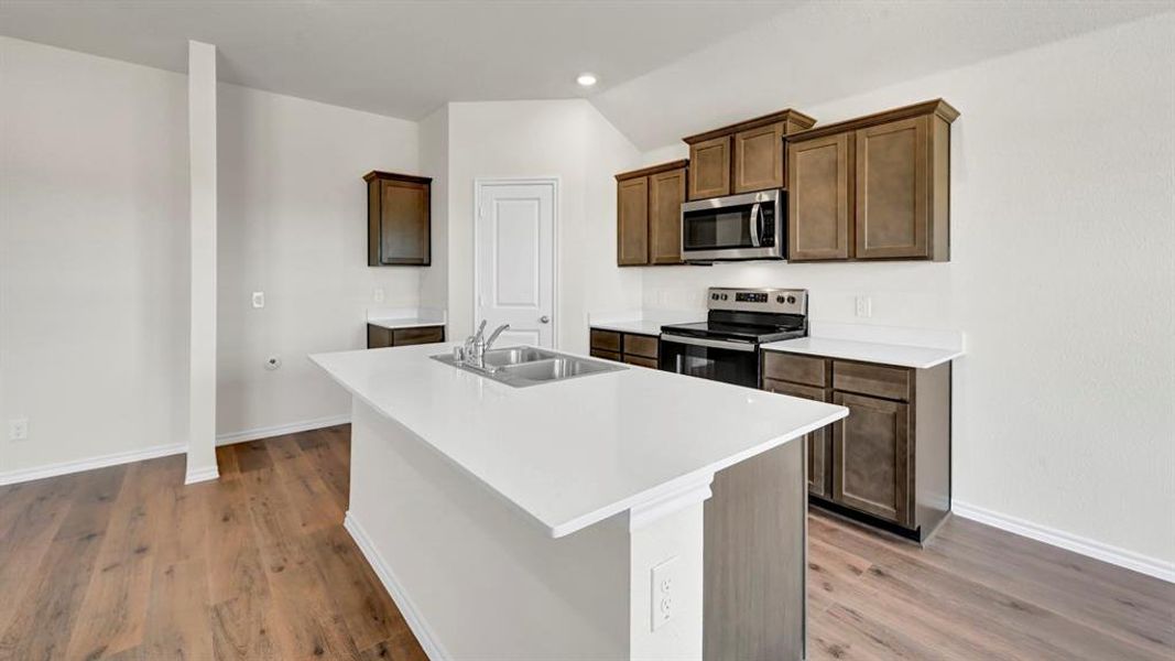Kitchen featuring a central island with a double basin sink, stainless steel appliances, dark wood-finish cabinetry, and light countertops