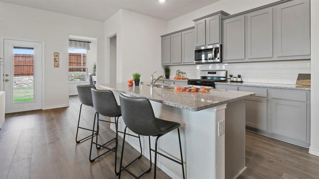 Kitchen featuring gray cabinets, light stone countertops, appliances with stainless steel finishes, decorative backsplash, and a kitchen breakfast bar