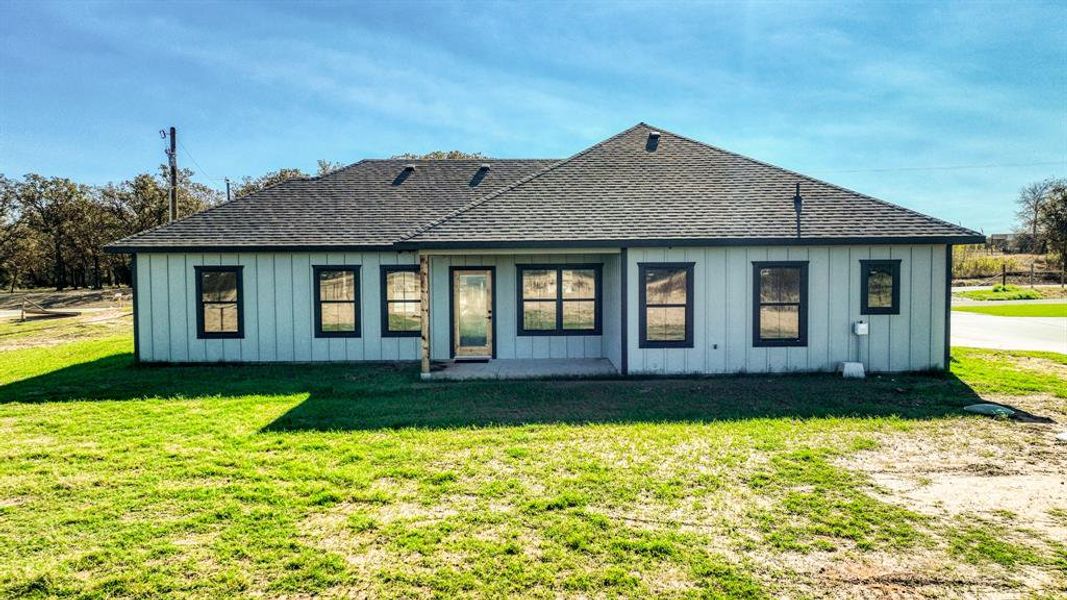 Back of property with a shingled roof, a patio, board and batten siding, and a yard