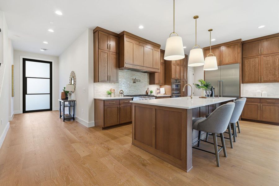 Kitchen with brown cabinetry, a breakfast bar area, decorative light fixtures, a kitchen island with sink, and light wood-type flooring