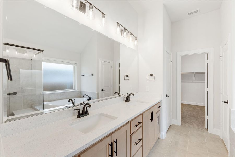 Master bathroom with double vanity, quartz countertop, glass shower, and walk-in closet doorway visible.