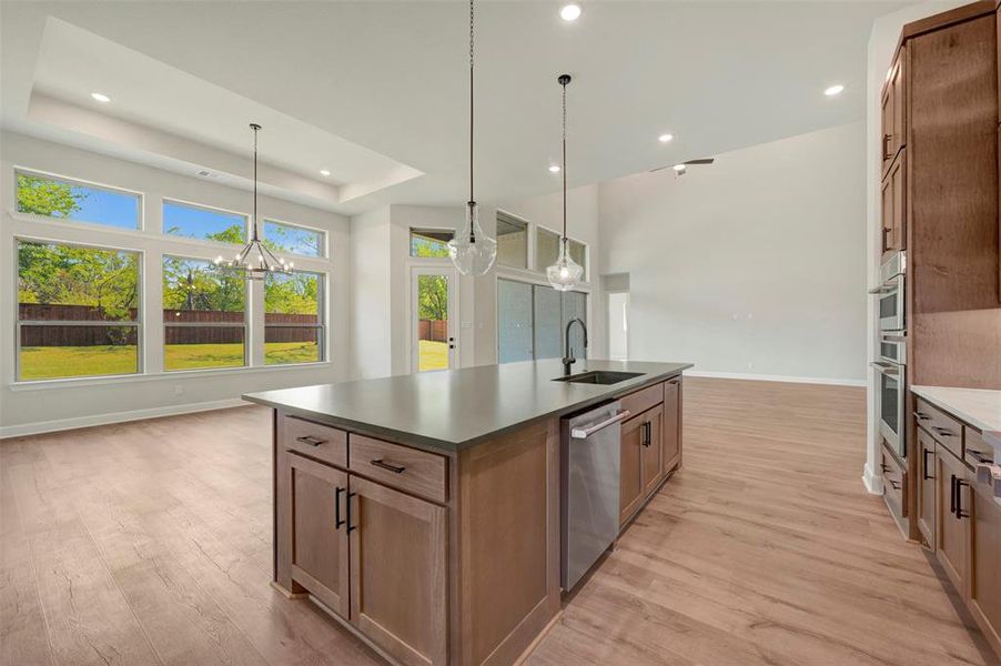 Kitchen featuring a center island with sink, light wood-style flooring, a tray ceiling, stainless steel dishwasher, and open floor plan