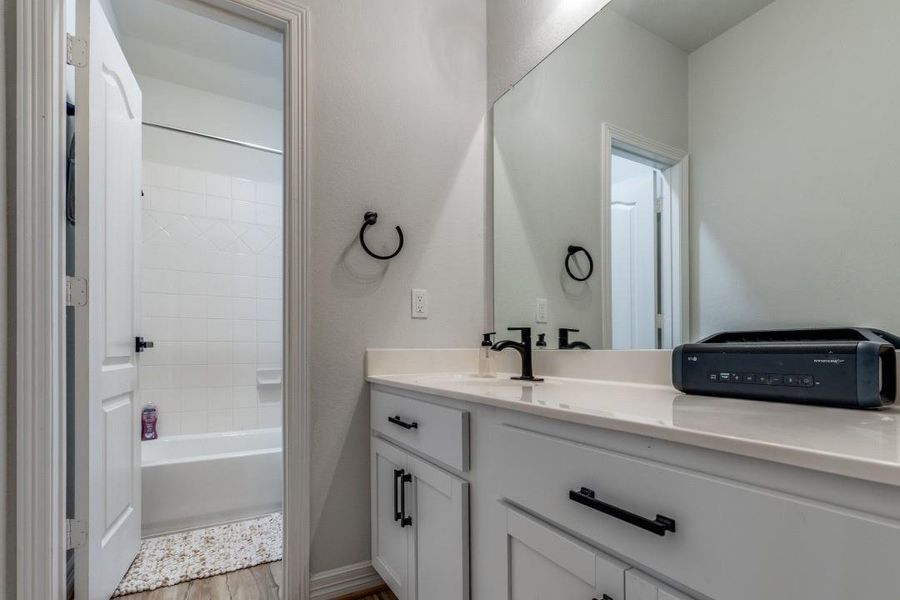 Modern bathroom with a dual-sink vanity, sleek black fixtures, and a large mirror. The space features a bathtub with a shower, white cabinetry, and a neutral color palette, creating a clean and inviting atmosphere.