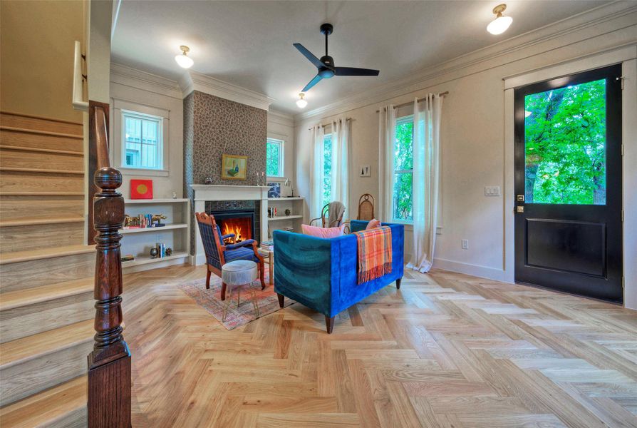 Herringbone hardwood floors extend through this inviting living room, featuring a cozy fireplace and built-in shelving.