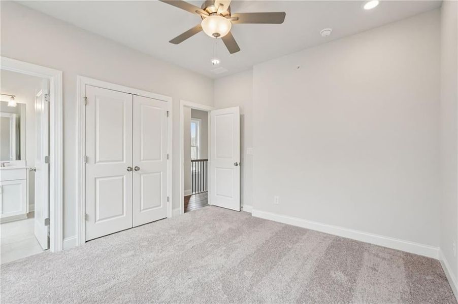 Unfurnished bedroom with light colored carpet, ceiling fan, connected bathroom, and a closet