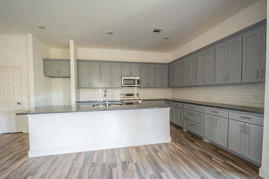 Kitchen featuring gray cabinets, stainless steel appliances, dark wood-style floors, and dark stone counters