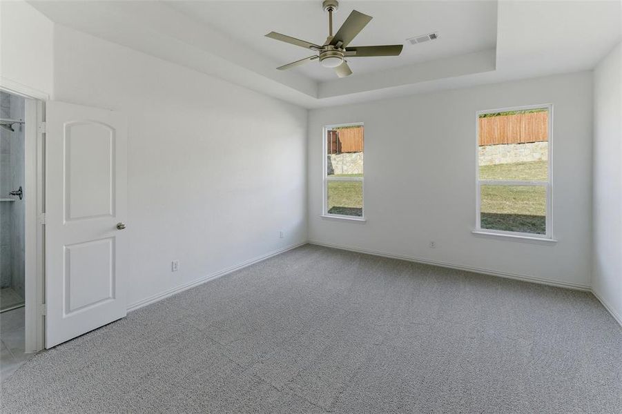 Empty room featuring light colored carpet, ceiling fan, and a tray ceiling