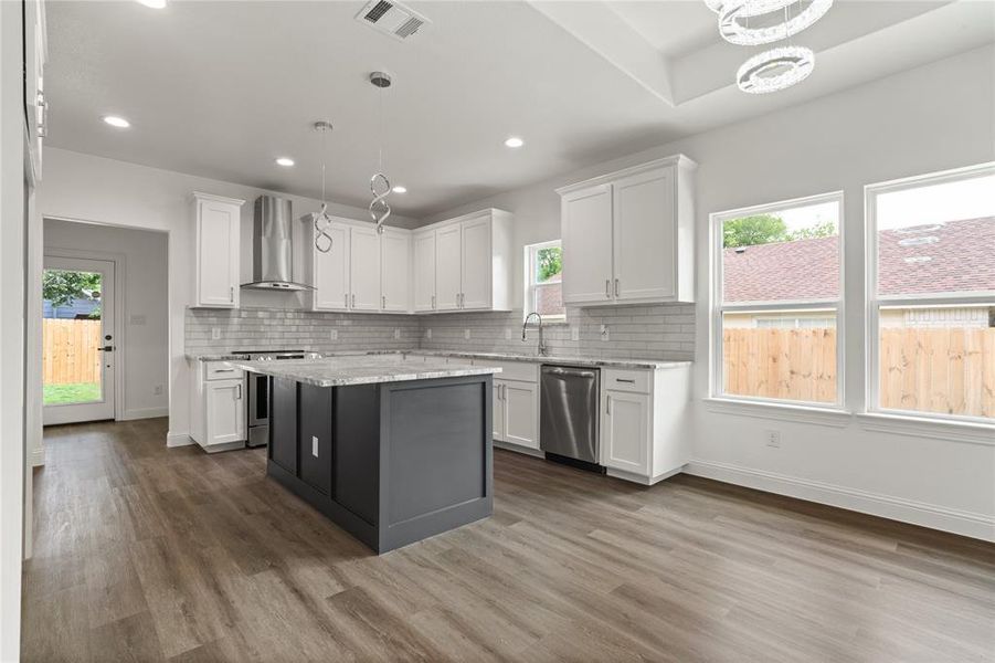 Open-concept kitchen featuring an island with a light-colored countertop, white cabinetry, stainless steel appliances, a subway tile backsplash, and recessed lighting
