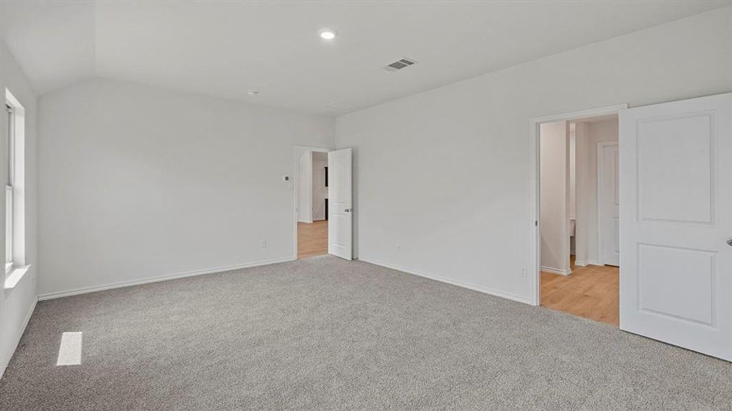 Spacious room featuring vaulted ceilings, light gray carpeting, and multiple doorways