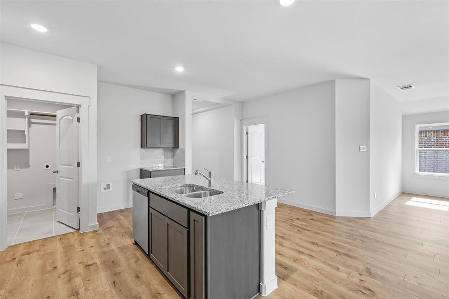 Kitchen featuring light stone countertops, light wood finished floors, a center island with sink, tasteful backsplash, and recessed lighting