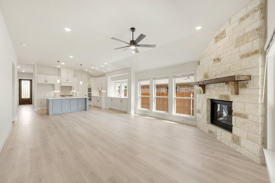 Open living area with stone fireplace, light wood floors, and open kitchen with blue island in background