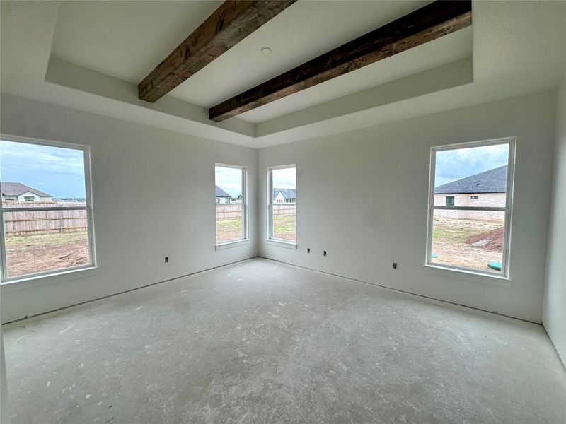 A spacious, naturally illuminated room awaiting personal touches, highlighted by rustic wood beam accents.