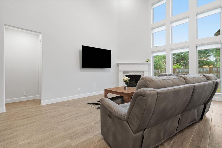 This living room features high ceilings and abundant natural light from large windows. It includes a cozy fireplace, sleek TV, plush seating, and stylish wood flooring, offering a welcoming and modern space. This living room features high ceilings and abundant natural light from large windows. It includes a cozy fireplace, sleek TV, plush seating, and stylish wood flooring, offering a welcoming and modern space.