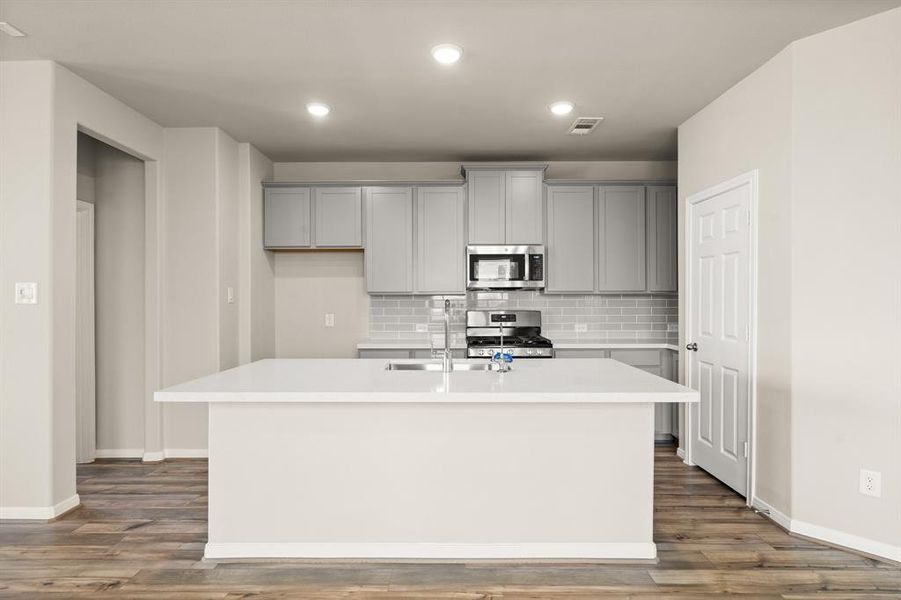 This light and bright kitchen features a large quartz island, white cabinets, a large sink overlooking your family room, recessed lighting, and beautiful backsplash.