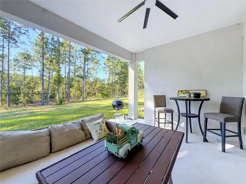 Covered patio featuring a painted concrete floor, ceiling-mounted fan, and exterior-facing structural pillars overlooking a lawn with mature trees