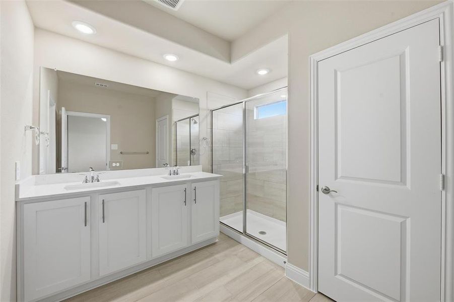 Full bath with double vanity, a shower stall, recessed lighting, and light wood-type flooring