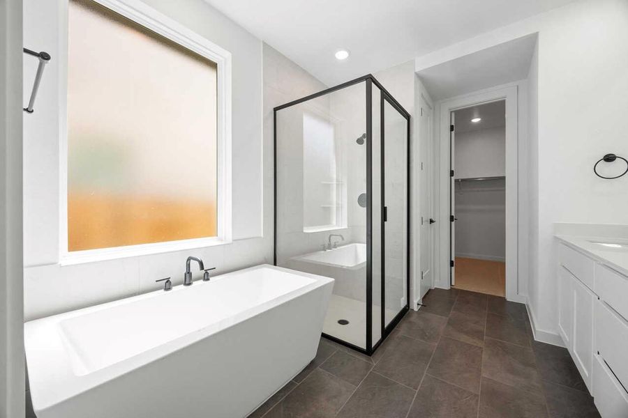Full bath with a stall shower, vanity, a soaking tub, a spacious closet, and dark tile patterned floors Full bath with a stall shower, vanity, a soaking tub, a spacious closet, and dark tile patterned floors