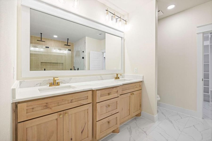 Full bathroom with double vanity, a stall shower, baseboards, marble finish floor, and a sink