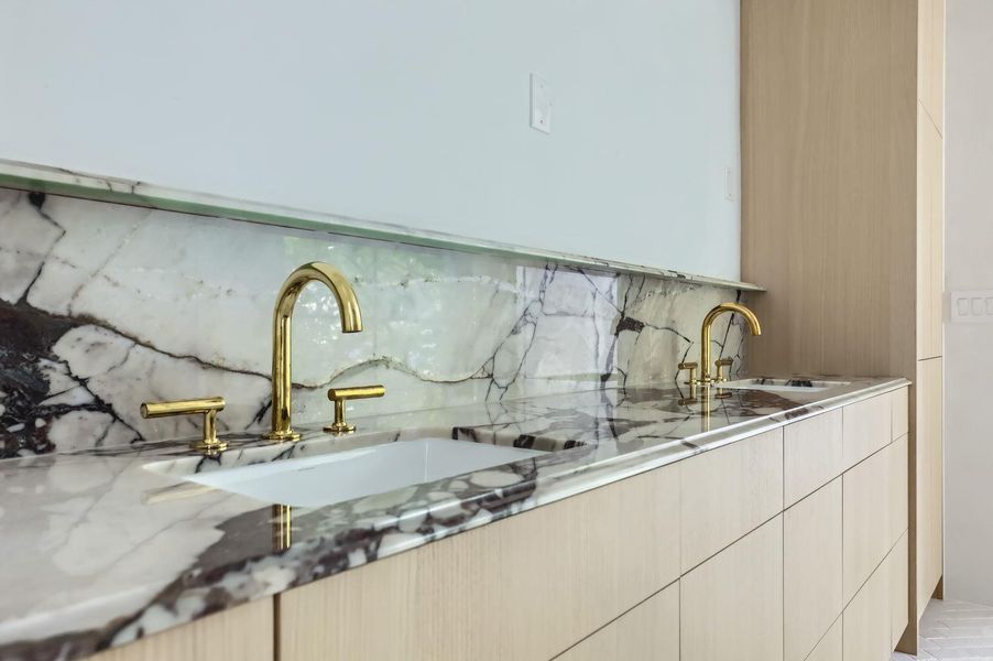 Luxurious gold fixtures adorn a marble countertop and backsplash, complemented by sleek wooden cabinetry.