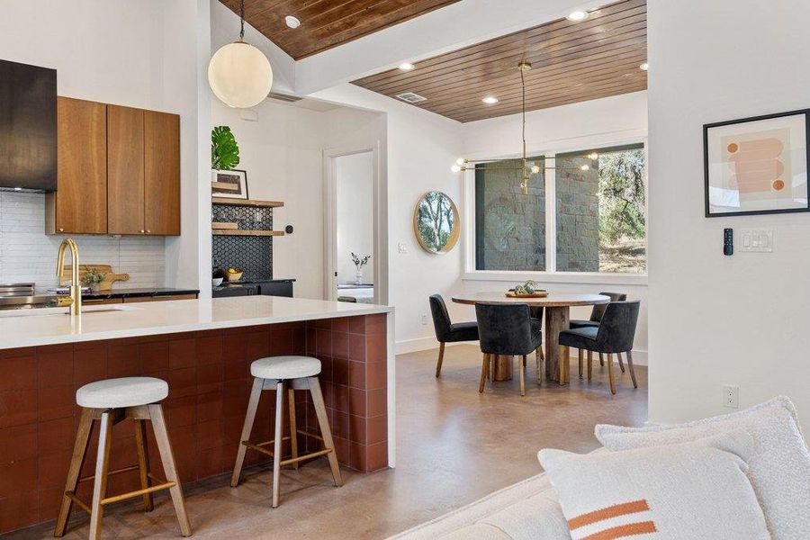 Kitchen featuring brown cabinetry, concrete floors, a breakfast bar area, decorative light fixtures, and modern cabinets