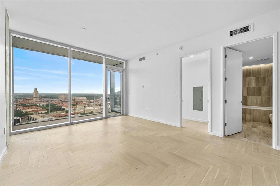 An open floor plan and floor-to-ceiling glass panels offering stunning city views, including the UT Campus building. Modern furnishings and neutral tones create a stylish and inviting space perfect for relaxation and enjoying the urban scenery.