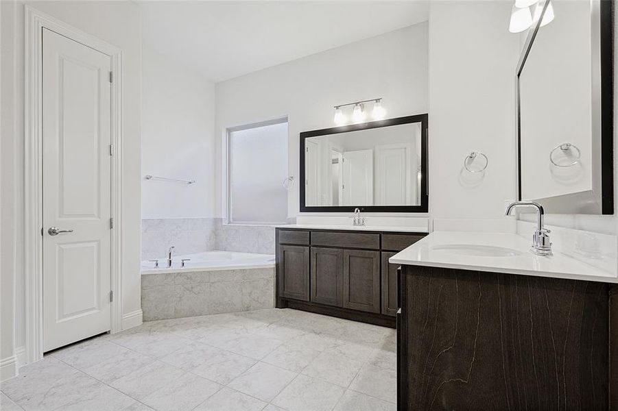 Bathroom featuring tile patterned flooring, vanity, and a relaxing tiled tub