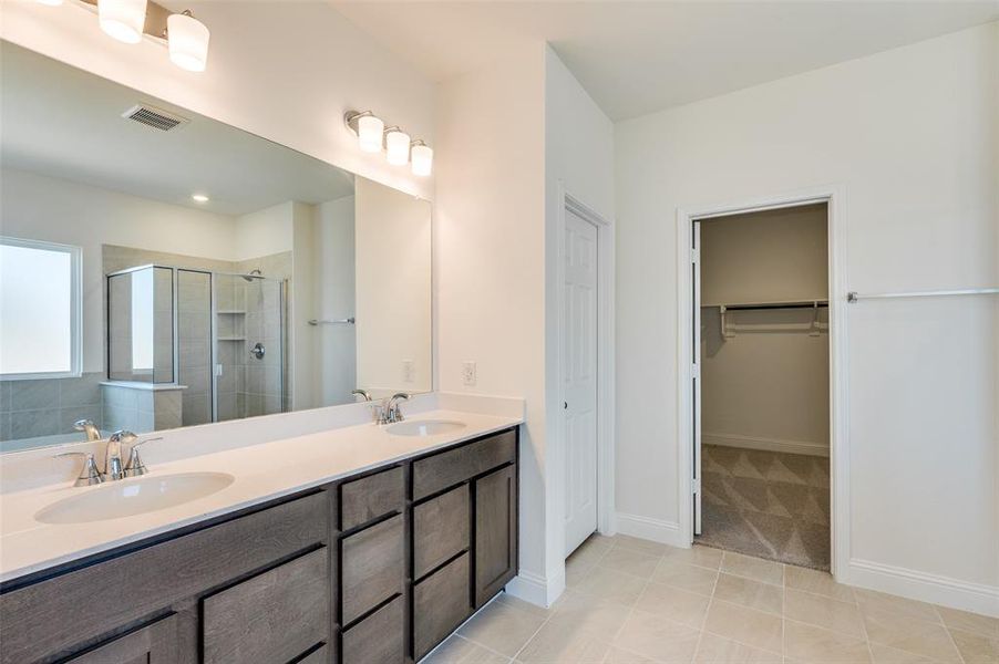Bathroom with a shower stall, double vanity, a spacious closet, and tile patterned flooring