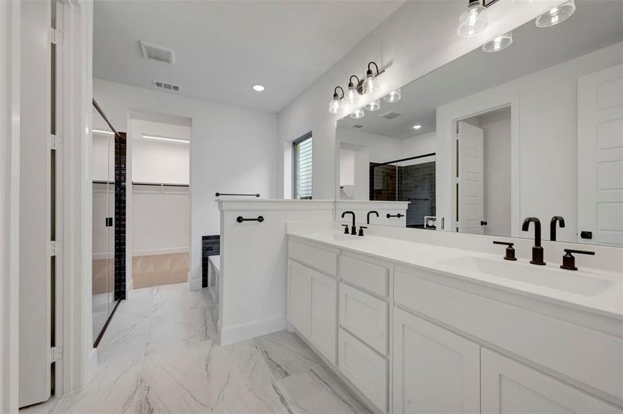 Bathroom featuring a dual vanity with white cabinetry, a large mirror, and matte black fixtures