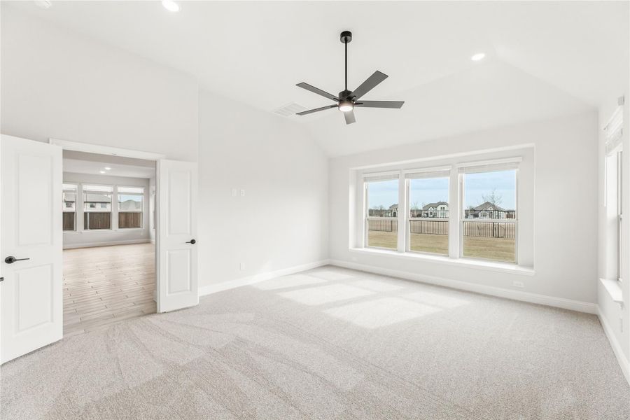 Spacious empty bedroom with vaulted ceiling, ceiling fan, carpet flooring, and large windows overlooking a backyard. Spacious empty bedroom with vaulted ceiling, ceiling fan, carpet flooring, and large windows overlooking a backyard.