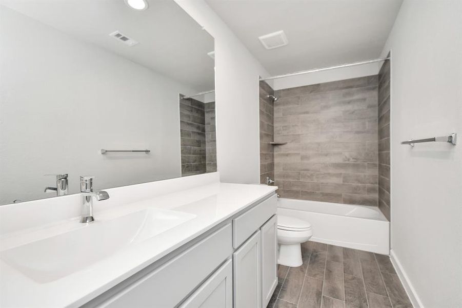 Secondary bath features tile flooring, bath/shower combo with tile surround, light stained wood cabinets, beautiful light countertop. Sample photo of completed home with similar floor plan. As-built interior colors and selections may vary.