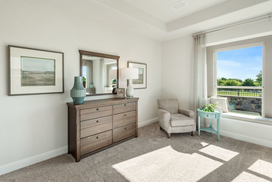 Bedroom with wood dresser, mirror, accent chair, and window seat overlooking outdoor view