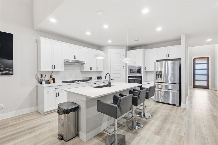 Kitchen with appliances with stainless steel finishes, decorative backsplash, white cabinetry, a breakfast bar, and recessed lighting