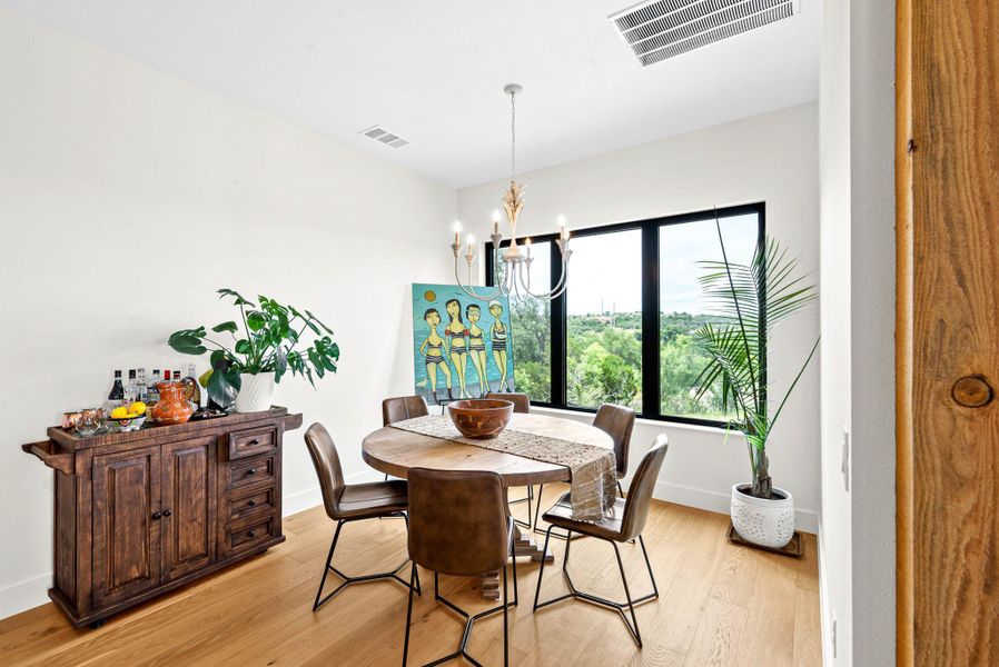 Warm wood flooring and large windows framing scenic green views define this inviting space.