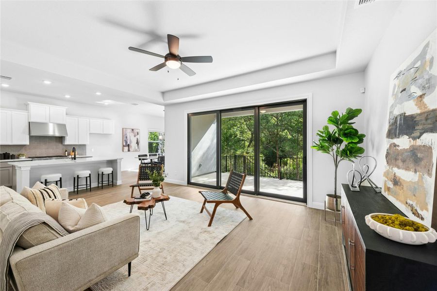 Living room with light wood-style flooring, a ceiling fan, and a raised ceiling Living room with light wood-style flooring, a ceiling fan, and a raised ceiling