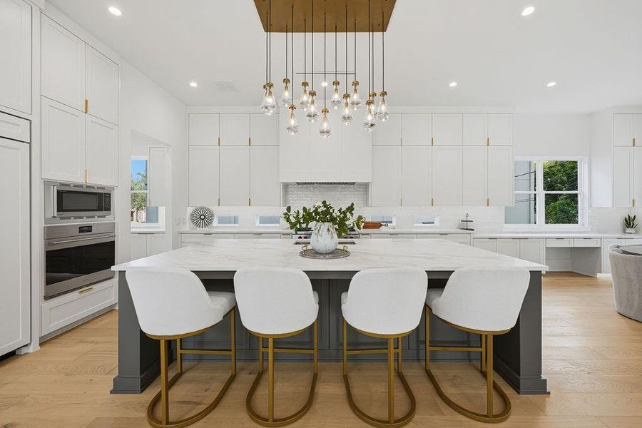The heart of the home is anchored by a dramatic multi-pendant "raindrop" chandelier, featuring delicate glass droplets and gold accents that create a shimmering focal point over the moody green-toned central island. This striking lighting design bridges the transition from the family room into a kitchen defined by its clean lines, airy volume, and high-end functional details.