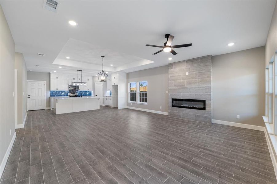 Unfurnished living room with a tiled fireplace, a tray ceiling, dark wood-type flooring, and ceiling fan with notable chandelier