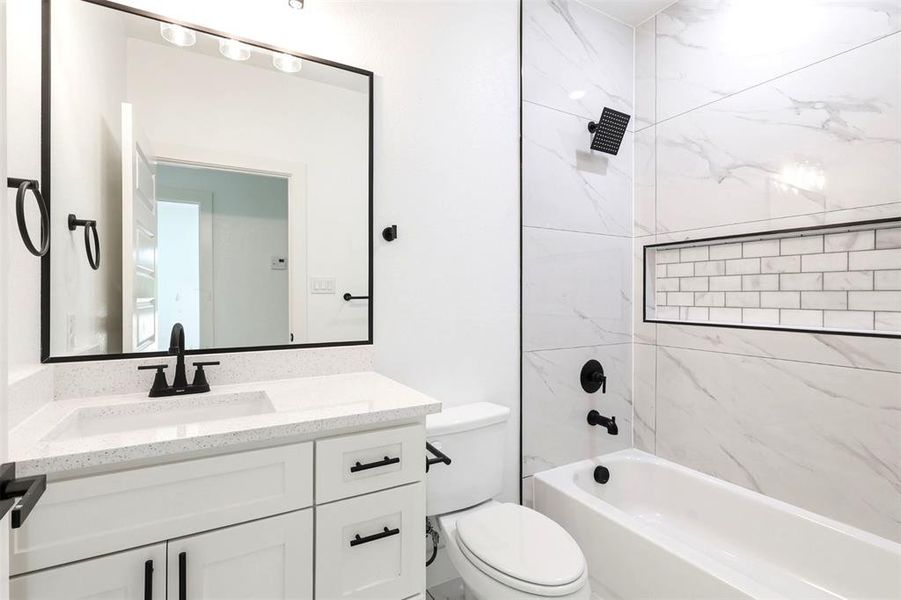 Bathroom featuring a white vanity with a light-toned countertop, a black-framed mirror, a black matte faucet, a built-in bathtub, and large-format tiled walls with a subway tile niche