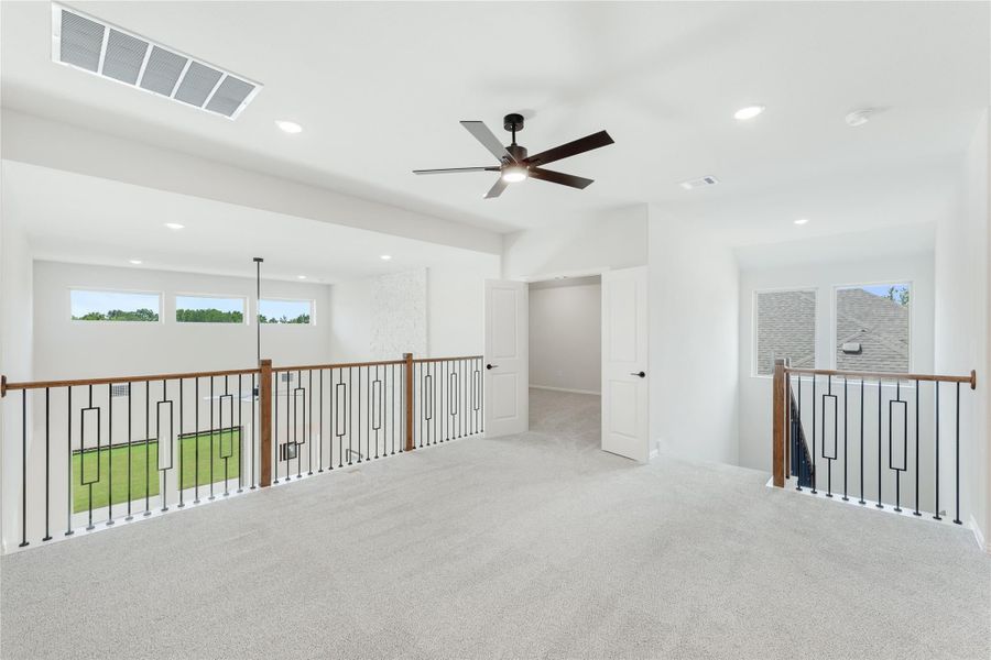 Open upstairs loft with carpet flooring, ceiling fan, and metal stair railings with wood handrails