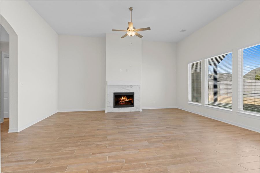 This expansive view of the main living area highlights the generous space, soaring ceilings, and rich wood like tile flooring, centered around a cozy gas fireplace and framed by large windows that bring in wonderful natural light and views of the backyard.