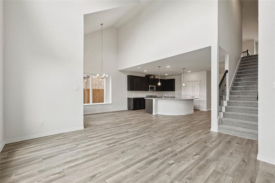 Unfurnished living room featuring an inviting chandelier, sink, light wood-type flooring, and high vaulted ceiling