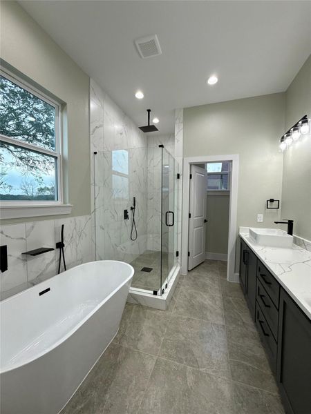 This modern bathroom features a sleek design with a freestanding tub, glass-enclosed shower, and dual sinks. It has elegant quartz accents, neutral tiles, and ample natural light from the window, creating a luxurious and inviting space.