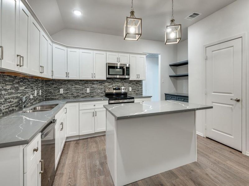 Kitchen with tasteful backsplash, appliances with stainless steel finishes, light hardwood / wood-style floors, decorative light fixtures, and a center island