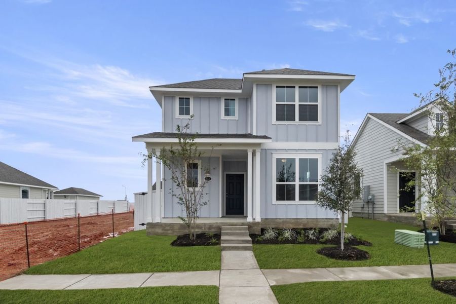 Image of exterior two story grey home with a black door, trees, green grass and a blue sky Image of exterior two story grey home with a black door, trees, green grass and a blue sky