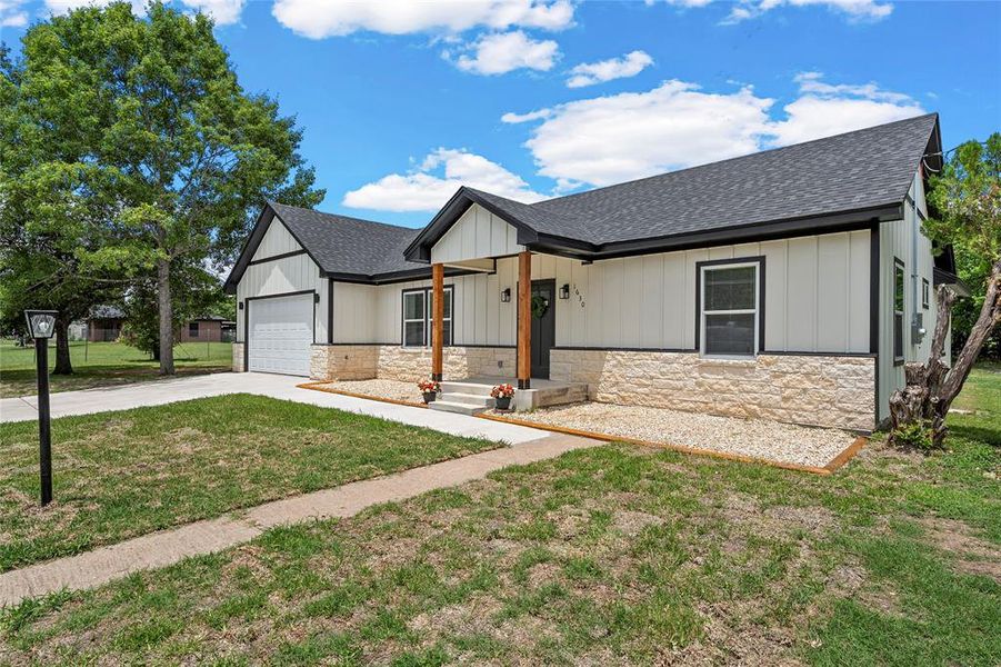 Contemporary exterior featuring white board and batten siding, a stone veneer foundation, and a dark shingle roof Contemporary exterior featuring white board and batten siding, a stone veneer foundation, and a dark shingle roof