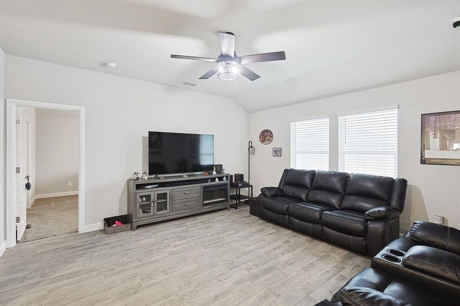 Living area featuring visible vents, light wood-style flooring, a ceiling fan, vaulted ceiling, and baseboards